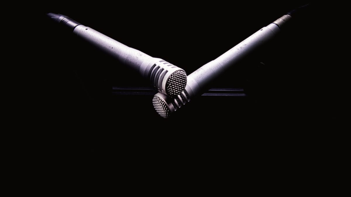Two studio microphones crossed in a dark recording booth